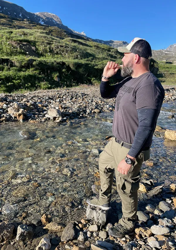 Florian Fischer von XCE Overlanding, der mit Leidenschaft bei der Arbeit ist, steht an einem Flusslauf in der Natur.